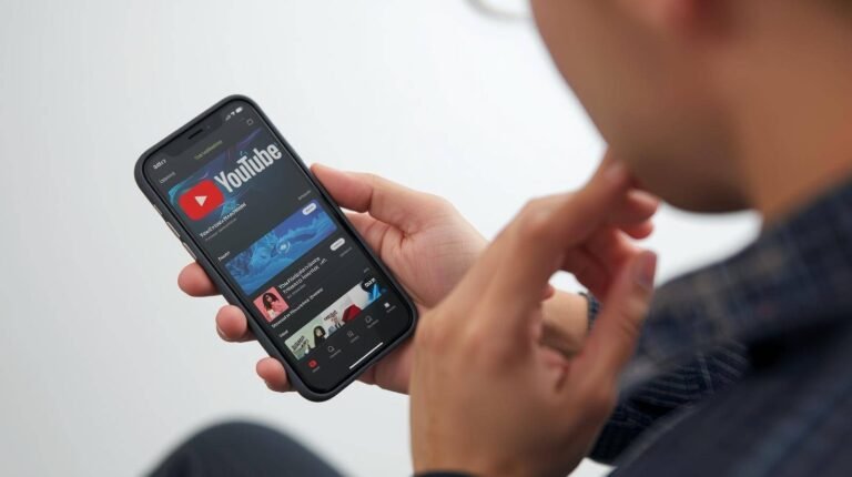A person is holding an iPhone and browsing the YouTube homepage, which displays various video and music content. The image visually relates to the problem: How Can I Download Music from YouTube to My iPhone?